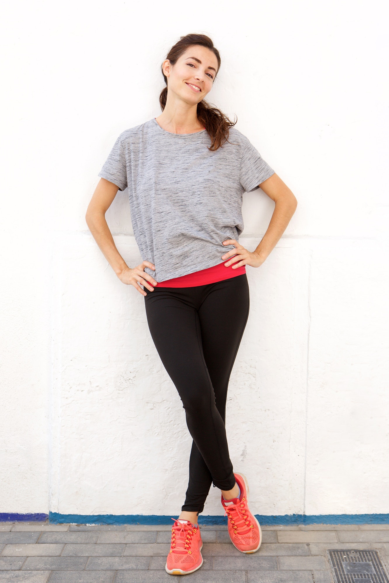 confident young woman in sportswear standing by a white wall